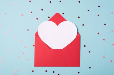 Üst katta, içinde sevgililer günü kartı olan paketlenmemiş zarfın yakın plan fotoğrafı var. Pastel arka planda parlak bir ışıltıyla taklit etmek için.