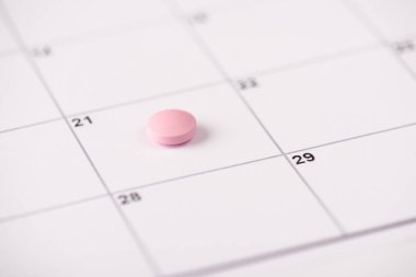 Zaman konseptinde uyuşturucu almak. Beyaz takvim hücresinin üzerinde duran pastel açık renkli pembe hapın görüntüsünü kapat