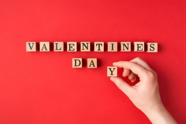 Sevgililer Günü konseptin kutlu olsun. Flatlay, kadın elinin son küpü sözcük gününe koyduğu en küçük görüntü fotoğrafını kapat, parlak kırmızı arkaplan