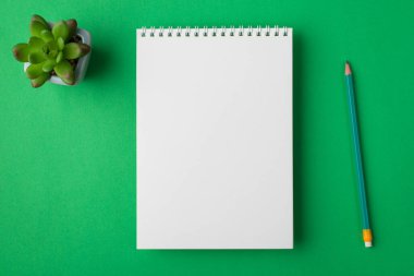 Yukarıda, dizayn metni için açık sayfası olan, parlak yeşil renkli masası olan spiral defterin yakın görünüm fotoğrafı var.