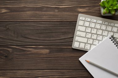 Üstte bilgisayar klavyesinin düz görünümü fotoğraf resmi boş bir not defteri ve koyu desenli ahşap zemin üzerinde duran bir kalem.