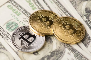 Yukarının üstünde Amerikan parası yığınının üzerinde duran altın ve gümüş bitcoin 'in yakın plan fotoğrafı var.