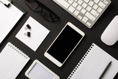 Üst taraftaki düz üst görünümde ofis aksesuarlarının etiketleri klasör klipleri düzenleyici bilgisayar gözlükleri boş boş dokunmatik ekranlı akıllı telefon izole edilmiş siyah fon.
