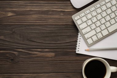 Üzerinde bilgisayar klavyesi fotokopi defteri sarmal kalem ve bir fincan sabah içeceği izole edilmiş koyu ahşap zemin.