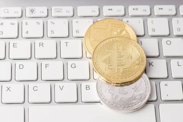 Yukarıda üstte klavyenin beyaz tuşlarına basılı duran altın ve gümüş bitcoin yığınının yakın görünüm fotoğrafı