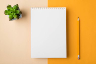 Tepede, dizayn edilmiş, yarı bej, yarı sarı masaüstü izole edilmiş, sulu yeşil bitkilerle dolu asgari dizayn sarmal defter fotoğrafı var.