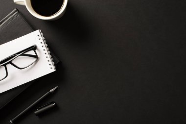 Yukarıdan bakıldığında profesyonel yöneticinin iş yeri fotoğrafı. Not defteri planlayıcı kalem ve bir fincan güçlü sabah içeceği. Boş arkaplan ve izole edilmiş siyah arkaplan.