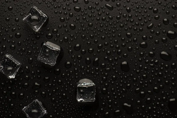 Top overhead above view photo of transparent ice cubes on black background with rain drops