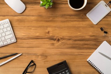 Üst düz görünümde ofis eşyalarının, bilgisayar faresi bardağı ve kahve klasörlü objelerin, not defterinin, boş uzay boşluğuyla izole edilmiş açık kahverengi masasının fotoğrafı yer almaktadır.