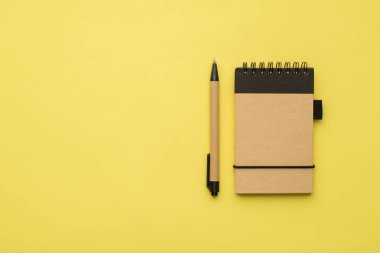 Sarı arkaplanda izole edilmiş organik defter ve kalem.