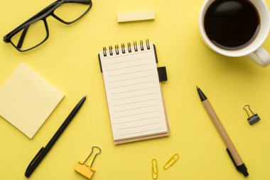 Not defterinin üstündeki fotoğraf. Kahve bardakları ve sarı arka planda izole edilmiş ataç.