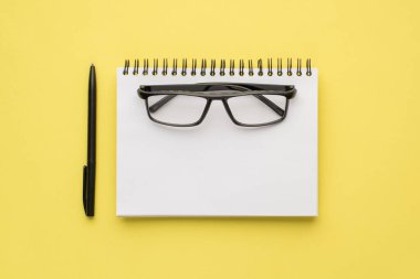 Not defteri gözlükleri ve sarı arka planda izole edilmiş siyah kalem.