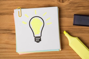 Ampul çizimi ve ahşap masa arkaplanındaki sarı işaretli çıkartma notlarının üst görünümü