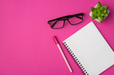 Açık planlama kalemli ve gözlüklü iş yerinin üst görünüm fotoğrafı kopyalanmış pembe arka planda