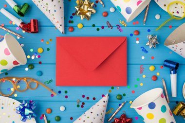 Doğum günü partisi bileşiminin üst görüntüsü orta spiral tüplerdeki kapalı kırmızı zarf şerit yıldızlar mumlar konfeti bardakları ve tabaklar izole edilmiş mavi ahşap masa zemininde.