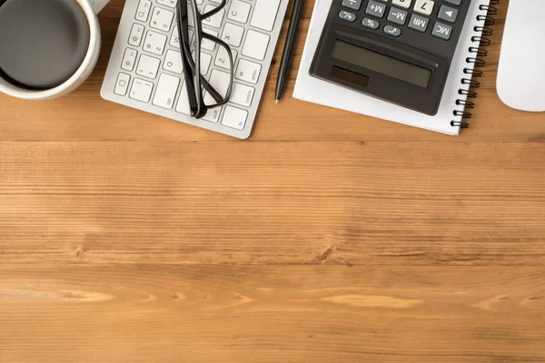 Overhead photo of notebook calculator glasses pen keyboard computer mouse and cup of coffee isolated on the wooden backdrop