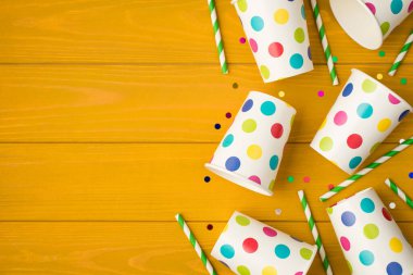 Bardakların yukarıdaki fotoğrafı parti tüpleri ve sarı ahşap arka planda izole edilmiş boş alanlı çok renkli konfetiler içeriyor.