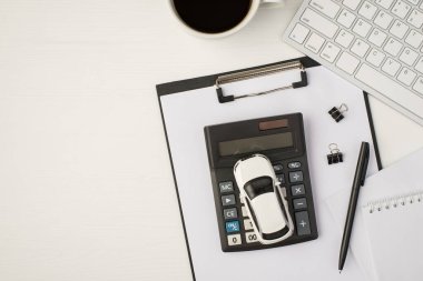 İş yerinin klavye not defteri, kahve kağıdı klasörü ve araba modelinin izole edilmiş beyaz arka planda hesap makinesinde çekilmiş en üst görünüm fotoğrafı.