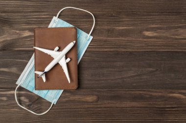 Deri pasaport kapağındaki uçak modelinin ve izole edilmiş ahşap masa arka planındaki tıbbi maskenin en iyi görüntüsü.