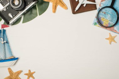 Pasaport kaplamalı oyuncak palmiye yaprağı ve izole edilmiş ahşap arka planda yıldız balıkları üzerindeki kamera haritası büyüteç uçak modeli.