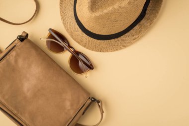 İzole edilmiş bej arka planda şapka gözlüğü ve deri çantanın fotosu.