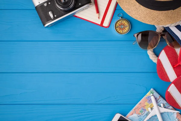 Overhead photo of camera notebook pencil compass hat sunglasses sandals map and airplane isolated on the blue background with empty space