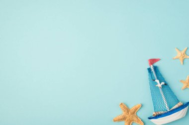 Martı ve yıldız balıklarıyla dolu gemi yatı oyuncağının en üst görüntüsü, kopyalanmış mavi arka planda.