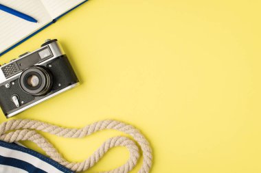 Mavi günlük fotoğraf makinesinin ve plaj çantasının üst görüntüsü izole edilmiş sarı arka planda ve kopyalanmış boşlukta