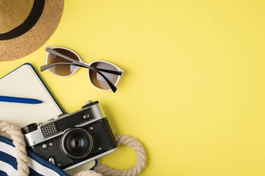 Baş örtüsü güneş gözlüğü plaj çantasının en üst görüntüsü mavi günlük kalemi ve kamera ile izole edilmiş sarı arkaplan ve telif alanı