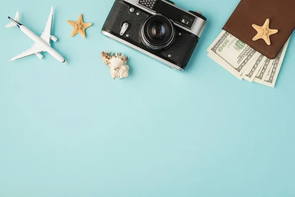 Top view photo of plane model camera seashell starfishes and passport cover with dollars on isolated pastel blue background with copyspace