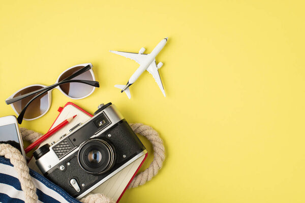 Над фото солнцезащитных очков сумка телефон камера карандаш тетрадь и самолет изолированы на желтом фоне с пустым местом