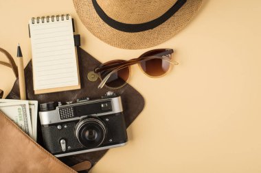 Fotokopi kitabı, kalem, güneş gözlüğü ve telif alanı olan izole edilmiş bej arka planda başlık takan açık deri çantanın en üstteki fotoğrafı.