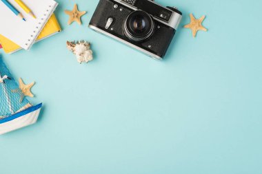 Not defterlerinin en üst görüntüsü kalemler oyuncak deniz kabuğu oyuncakları ve izole edilmiş pastel mavi arka plan üzerinde kamera.