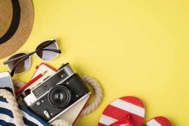 Güneş gözlüğü, fotoğraf makinesi, not defteri, kalem ve sandaletler. Sarı arka planda izole edilmiş ve boş alan var.