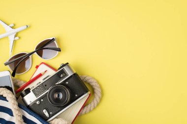 Güneş gözlüklü, telefon çantalı, not defteri, kalem ve uçak telif uzaylı sarı arka planda izole edilmiş.