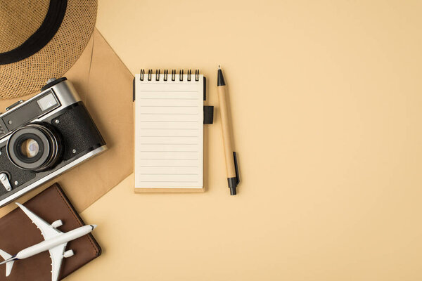 Top view photo of sunhat pen planner camera plane model passport cover on craft paper envelope on isolated beige background with copyspace