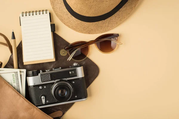 Fotokopi kitabı, kalem, güneş gözlüğü ve telif alanı olan izole edilmiş bej arka planda başlık takan açık deri çantanın en üstteki fotoğrafı.