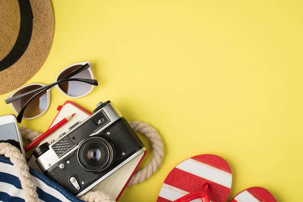 Güneş gözlüğü, fotoğraf makinesi, not defteri, kalem ve sandaletler. Sarı arka planda izole edilmiş ve boş alan var.