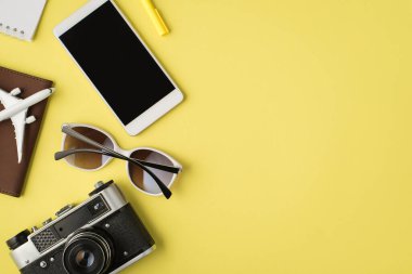 Akıllı telefon görüntüleme dizüstü bilgisayar kalem, güneş gözlüğü kamera ve uçak modeli, izole edilmiş pastel sarısı arka planda, kopyalanmış