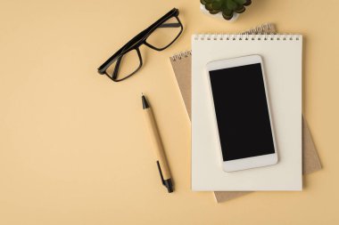 Not defterlerindeki akıllı telefon görüntüsünün üst görünümü. Bitki ve gözlük izole edilmiş bej arkaplandadır.