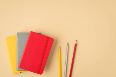 Kapalı üç planlayıcının en üstteki fotoğrafı. İzole edilmiş bej arka planda sarı gri ve kırmızı kalemler.