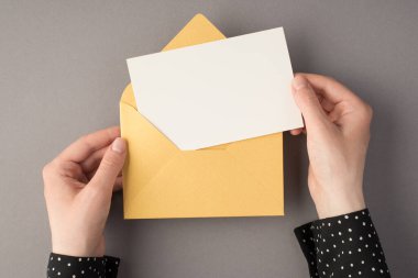 Kadın ellerinin açık pastel sarı zarf ile izole edilmiş gri arkaplan ve boş alan içeren beyaz bir zarf tuttuğu ilk kişi fotoğrafı.