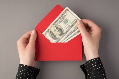 Üstten bakıldığında, kırmızı zarf tutan ve gri arka planda 100 dolarlık banknotlar tutan ilk kişi.