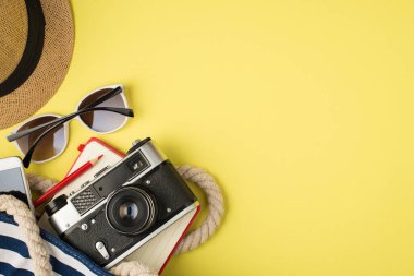 Şapka, güneş gözlüğü, telefon çantası, fotoğraf makinesi, not defteri ve sarı arka planda izole edilmiş boş alan.