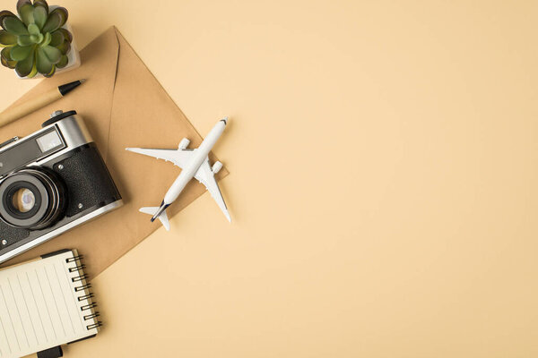 Top view photo of plant pen copybook camera and plane model on craft paper envelope on isolated beige background with copyspace