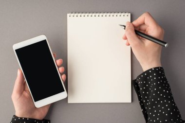 Kadının ellerinin kalem ve akıllı telefon tutarken çekilmiş ilk resmi izole edilmiş gri arka planda ve boş alanda.