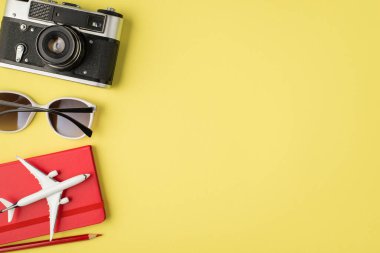 Kameranın en üstteki fotoğrafı güneş gözlüğü kalem ve uçak modeli kırmızı defter üzerinde izole edilmiş pastel sarı arkaplan ve telif alanı