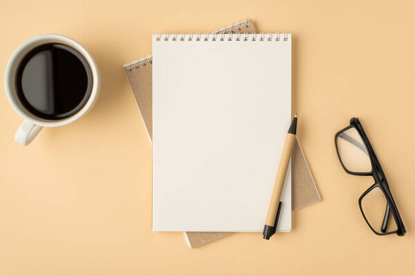 Top view photo of notepads and pen in the middle cup of coffee glasses on isolated beige background with blank space