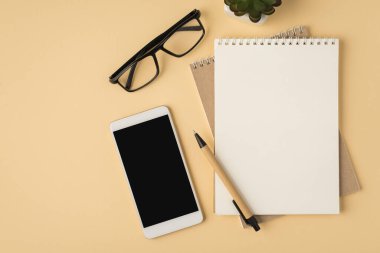 Akıllı telefon görüntüleme fotoğrafının üst görüntüsü çiçek saksısı defterleri kalem ve gözlüklerin izole edilmiş bej arkaplanı ve telif alanı