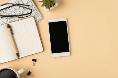 Telefon görüntüsü düzenleyici kalem bardaklarının üst görüntüsü klavye klasörleri üzerinde kahve fincanı ve izole edilmiş bej arka planda çiçek saksısı ve kopyalanmış bej alan